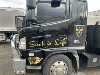 The side of the black tilt tray truck with gold lettering on the door